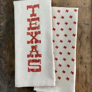 Folded Texas kitchen towel with vertical orange TEXAS print and orange state shapes