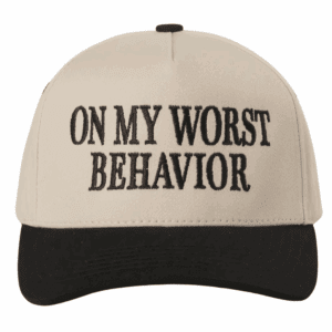 A cream and black trucker hat with bold black embroidery reading “ON MY WORST BEHAVIOR” on the front panel.