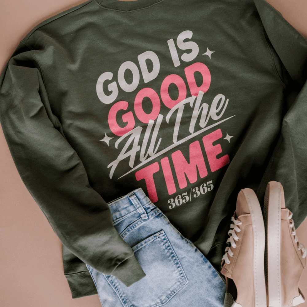 Flat lay of a forest green sweatshirt with bold white and pink lettering that reads "God is Good All The Time 365/365"