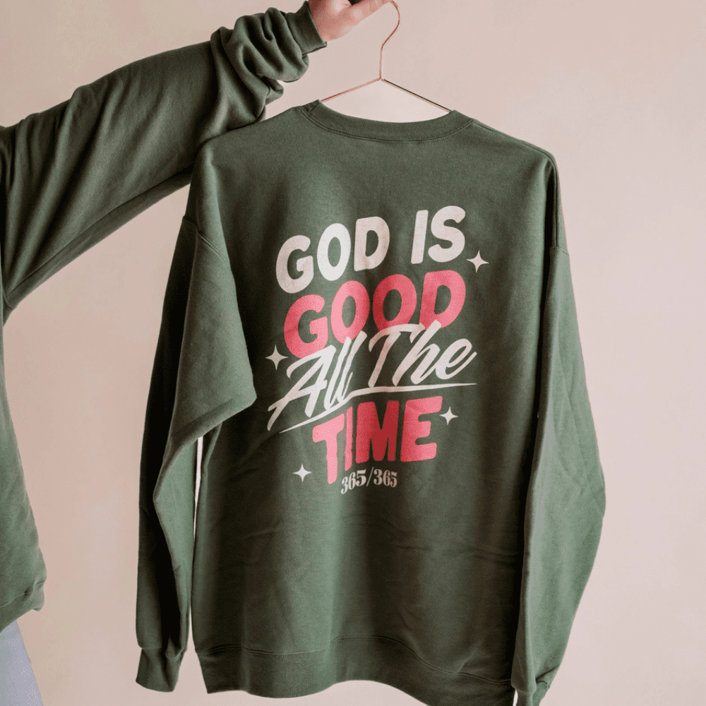 Green sweatshirt hanging on a gold hanger with large back print: "God is Good All The Time 365/365"