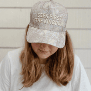 Close-up front view of woman wearing a camouflage-pattern Seek First The Kingdom hat