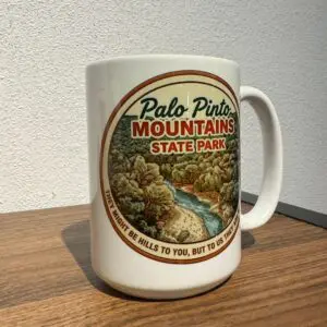Side angle of ceramic Palo Pinto Mountains State Park mug showing trees, river, and full quote