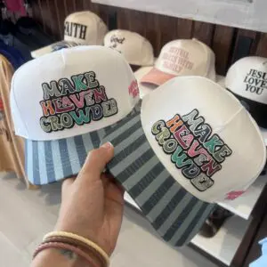 White trucker hat with colorful embroidered Make Heaven Crowded lettering and blue striped bill.