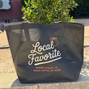 Black oversized tote bag featuring Local Favorite Parker County Peach Festival graphic with peach illustration.