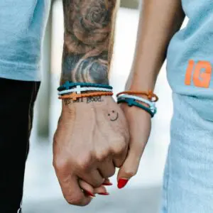 Couple wearing the Daybreak Cross Bracelet Set by In God We Must in teal, white, and camel