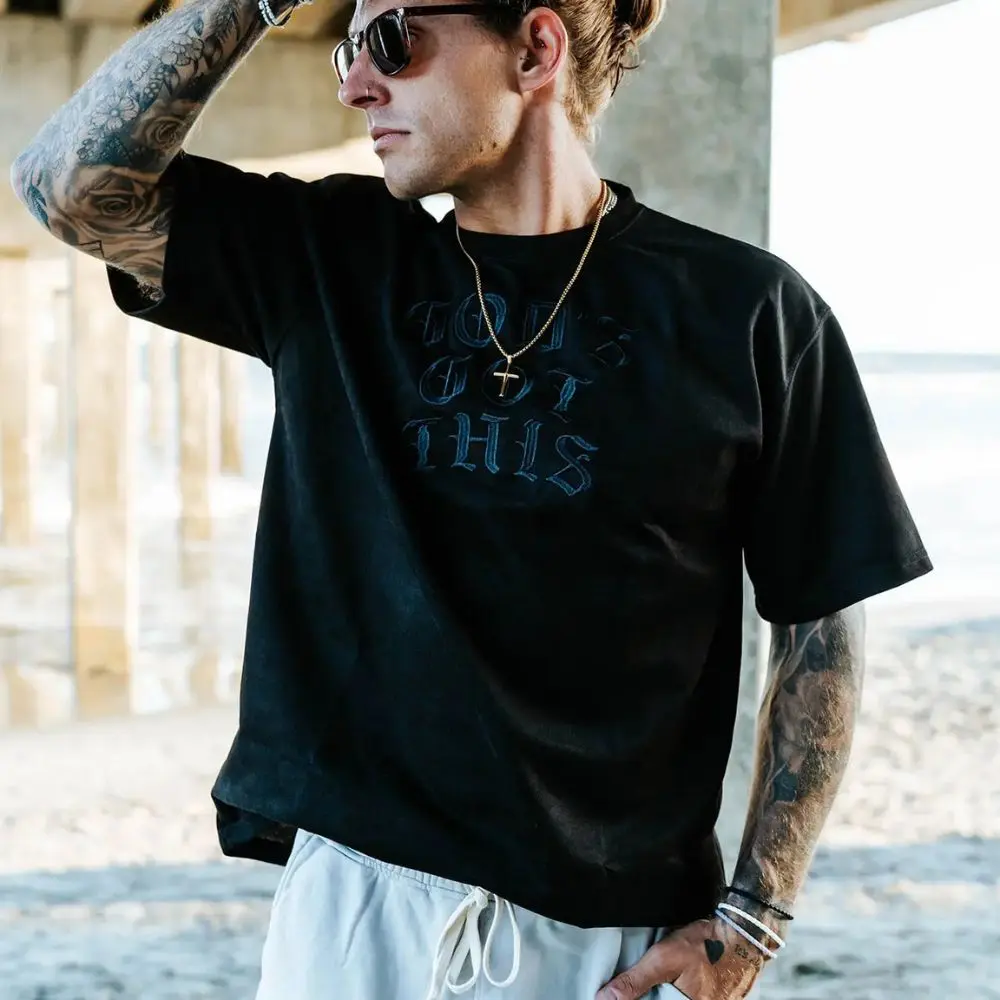 Person wearing Gold Cross Necklace by In God We Must with black embroidered shirt