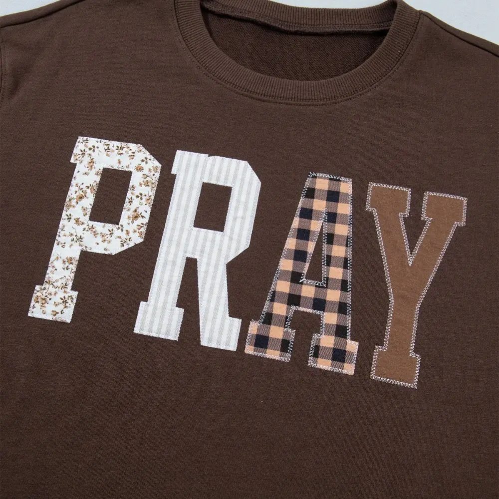 Close-up of patchwork PRAY lettering on brown Christian sweatshirt