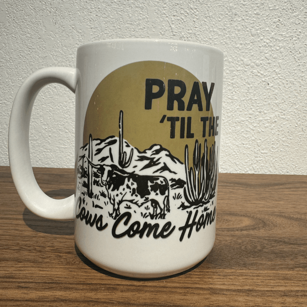 White ceramic mug with western landscape and "Pray 'Til The Cows Come Home" text