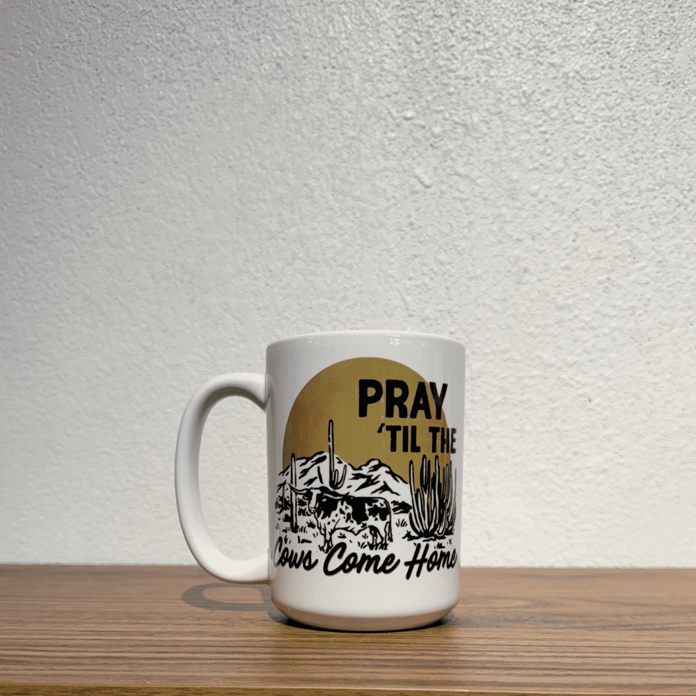 White ceramic mug with western landscape and "Pray 'Til The Cows Come Home" text