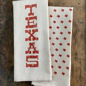 Folded Texas kitchen towel with vertical orange TEXAS print and orange state shapes