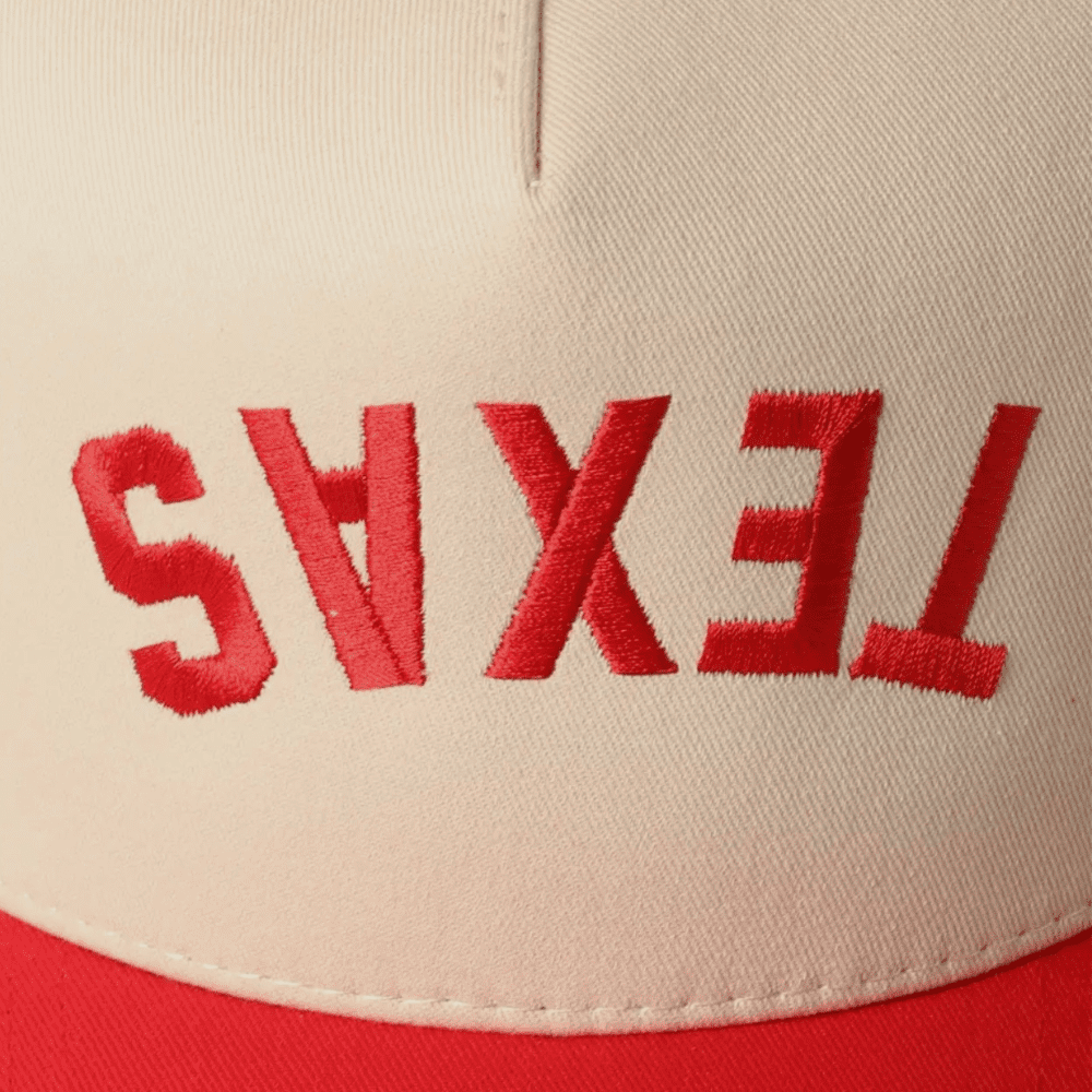 Detailed close-up of red “TEXAS” embroidered upside down on cream fabric