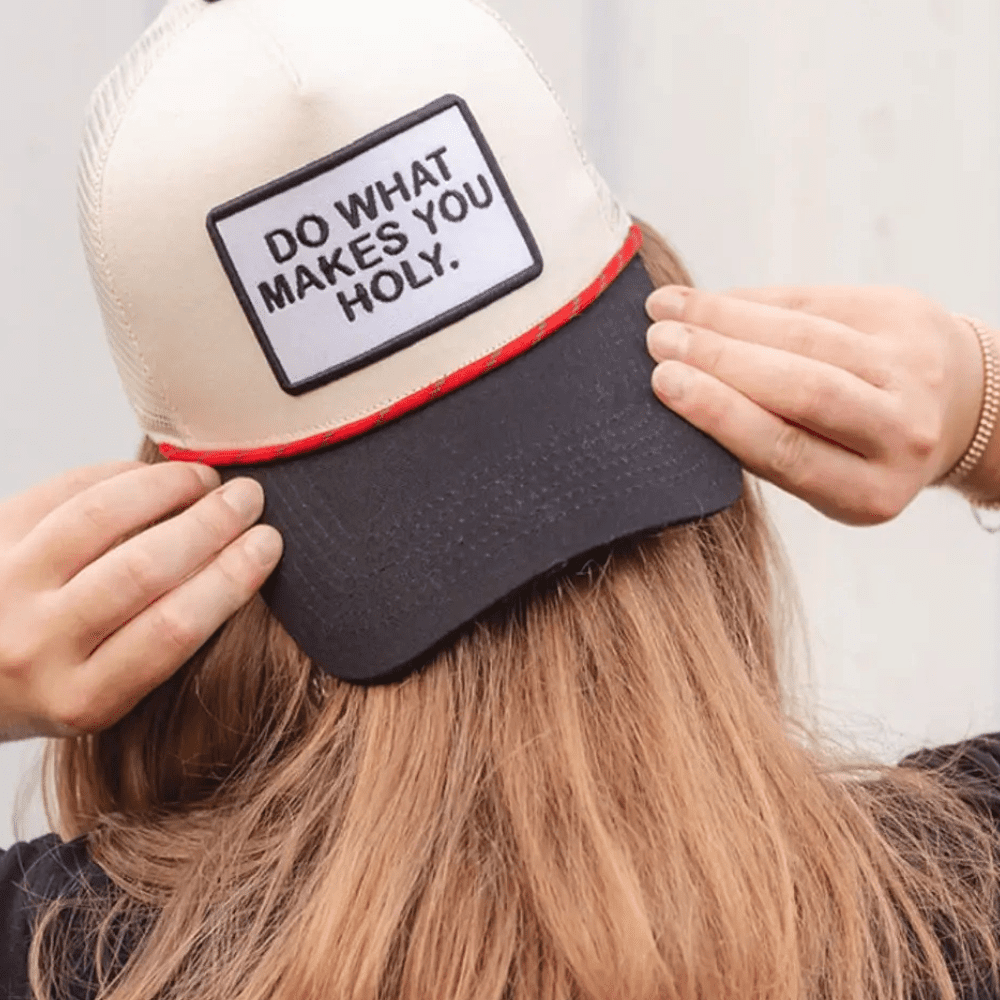Woman smiling while wearing a “Do What Makes You Holy” embroidered hat outdoors