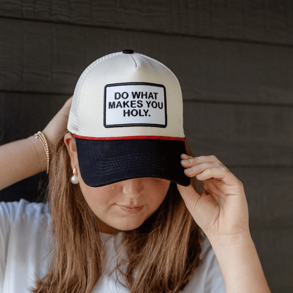 Woman wearing a cream and black snapback hat with embroidered patch that reads “Do What Makes You Holy”