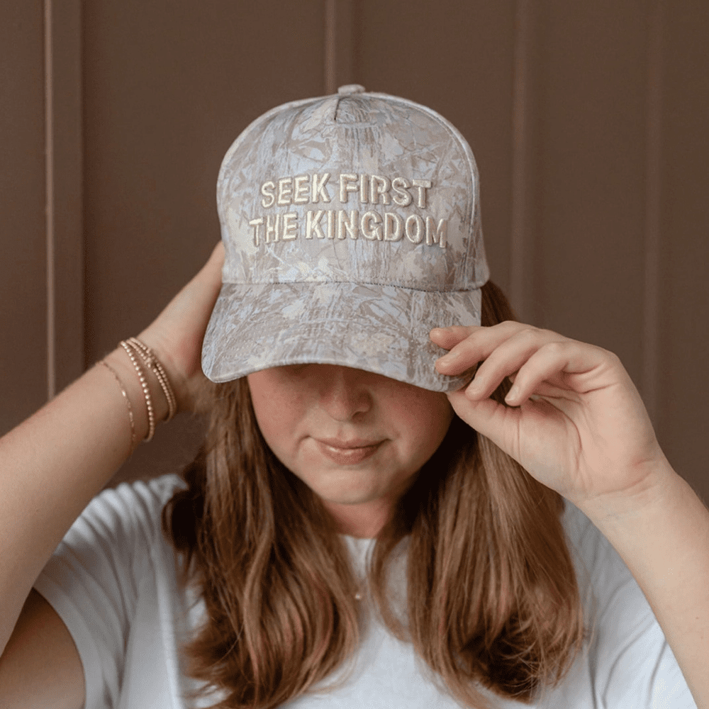 Woman tilting Seek First The Kingdom hat in a shaded setting